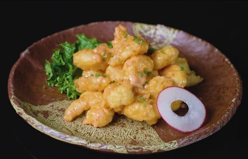 Crispy fried shrimp coated in a creamy orange sauce, garnished with lettuce and a radish slice.