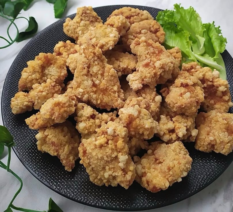 Crispy fried chicken bites on a black plate, garnished with fresh green lettuce.